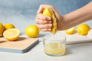 hand squeezes lemon into cup, making lemonade